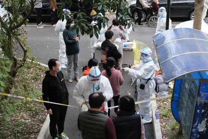 shutterstock_2140295957 Christian Jones and others wait at an outdoor COVID-19 testing site with staff in protective suits