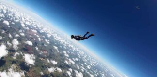 Skydiver freefalling above clouds and landscape