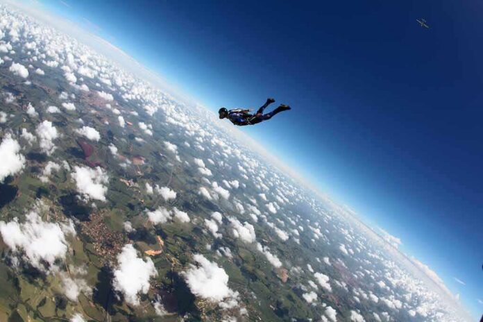 shutterstock_2253946721 Skydiver freefalling above clouds and landscape