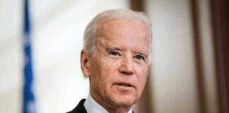 Joe Biden in a suit and purple tie speaking indoors