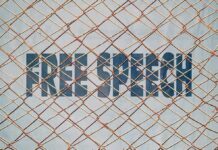 Rusty chain-link fence over bold text on a wall