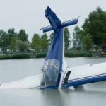 A submerged airplane partially in a lake with trees in the background
