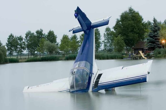 A submerged airplane partially in a lake with trees in the background