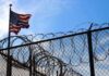 American flag near barbed wire fence against blue sky