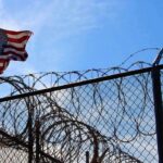 American flag near barbed wire fence against blue sky