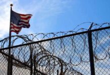 ICE Detention Death Sparks Outrage American flag near barbed wire fence against blue sky