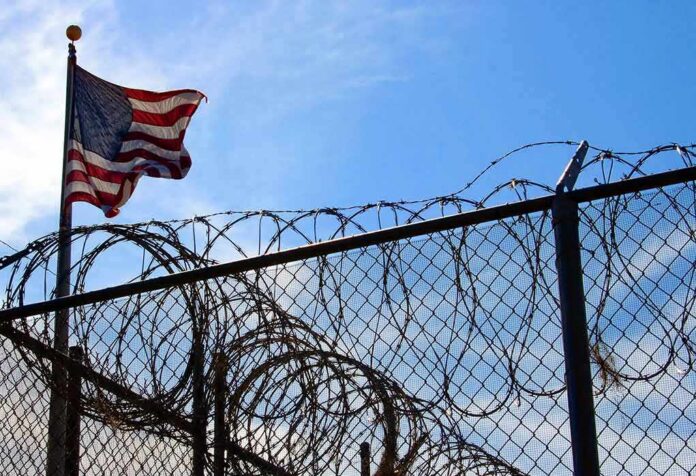 American flag near barbed wire fence against blue sky