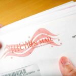 Election Offices Hit With Mystery Powder A hand holding an envelope labeled Official Election Mail