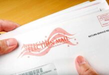 Election Offices Hit With Mystery Powder A hand holding an envelope labeled Official Election Mail