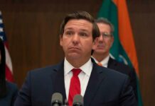 Storm Threat: DeSantis Orders Action Ron DeSantis at a press conference podium in a suit and red tie