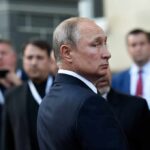 Vladimir Putin in a dark suit looking over his shoulder amid a crowd
