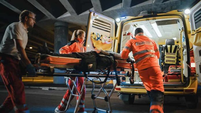 shutterstock_1878018001 Paramedics load a patient on a stretcher into an ambulance at night