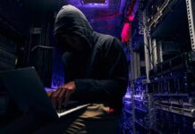 Hooded person using a laptop in a dark server room