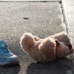 Teddy bear and single blue sneaker on a sidewalk