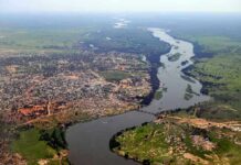 Killer Surge Shreds Bridges In Minutes Aerial view of a river winding through a town and green fields